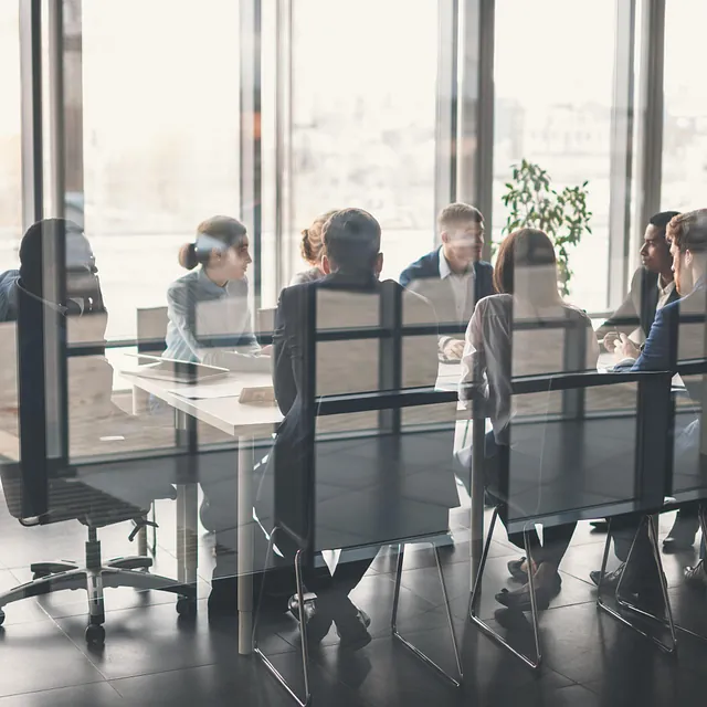 Møte i glasskontor, team diskuterer rundt bord.